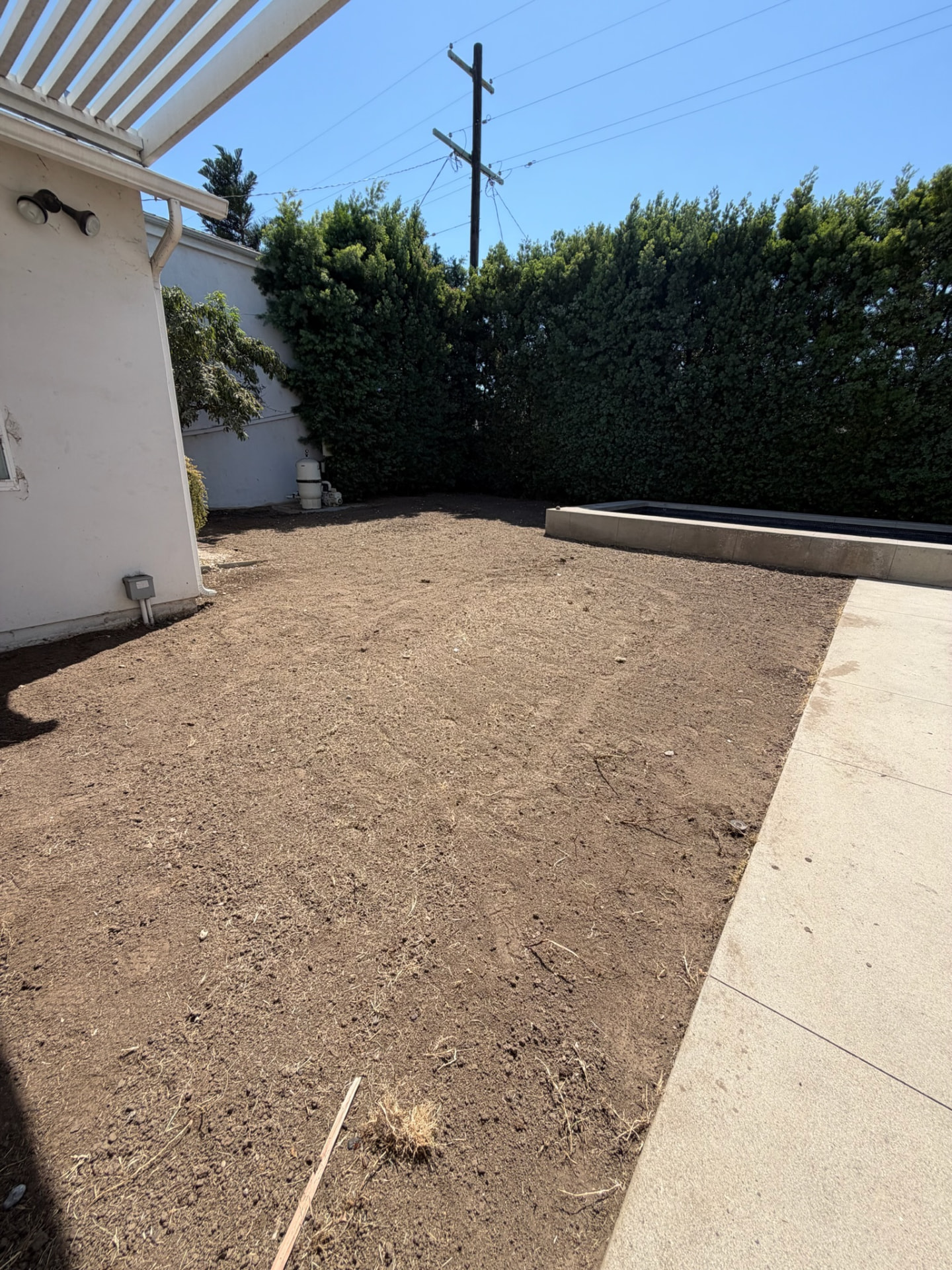 Bare graded dirt backyard beside a pool before sod installation